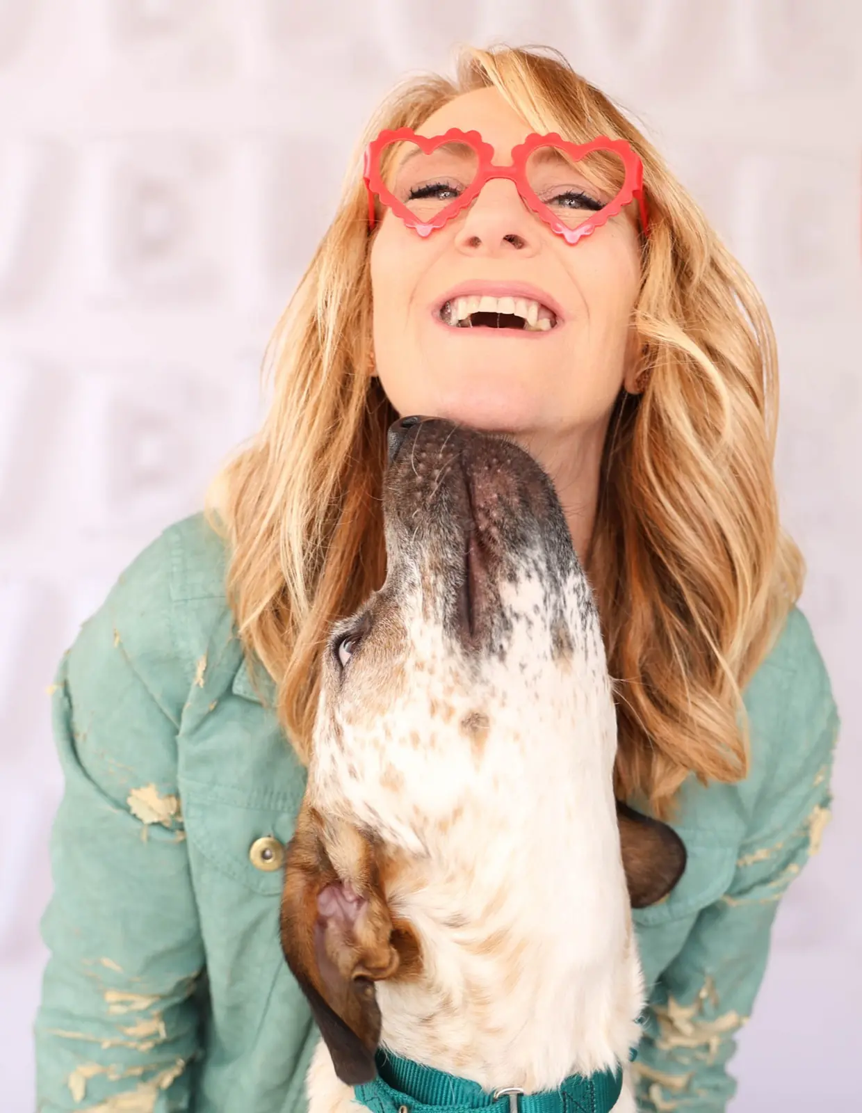Juli smiling, wearing red heart-shaped glasses and holding a brown-and-white dog